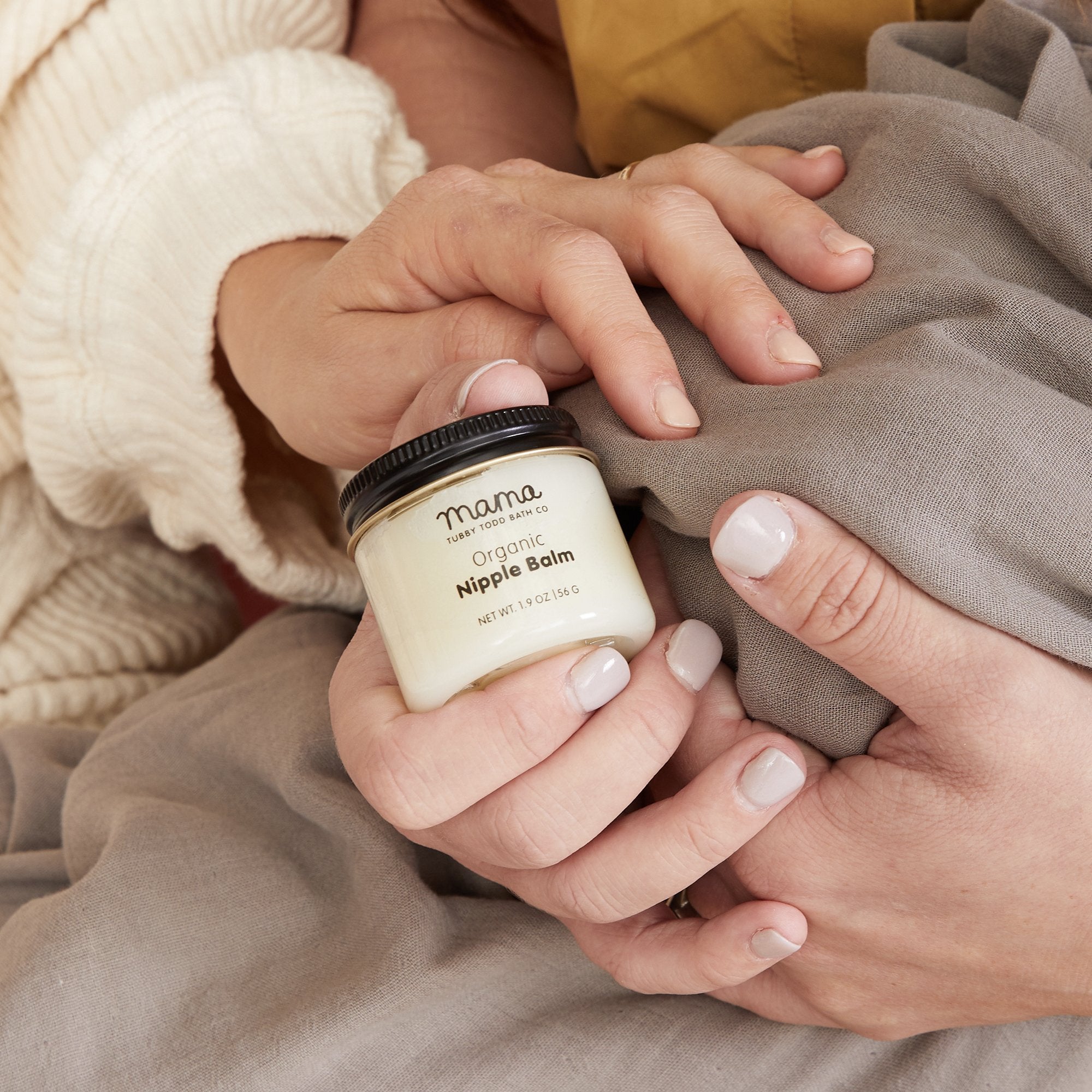 Mothers hand holding Nipple Balm jar